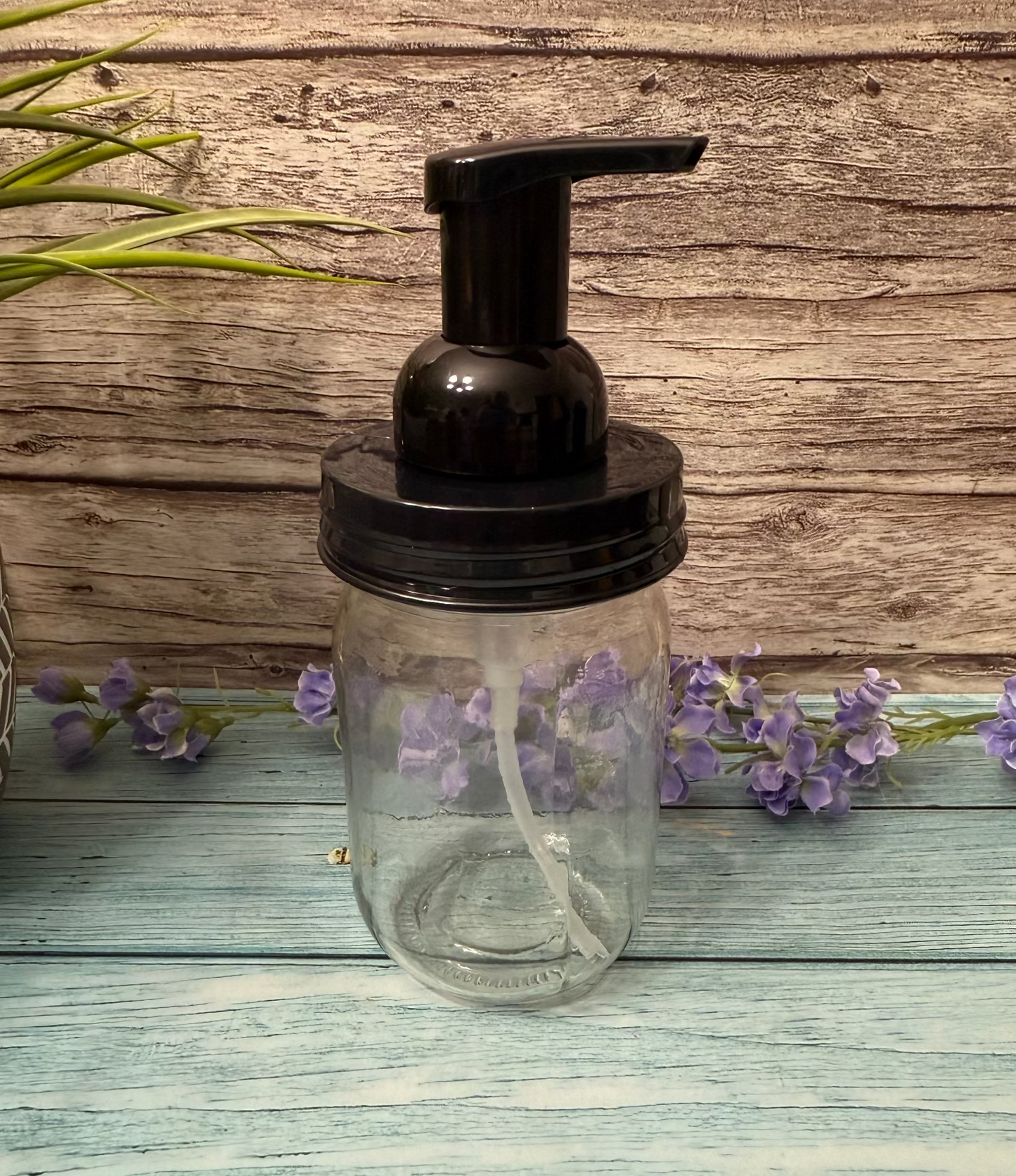 Clear glass soap dispenser with black pump on a wooden surface with lavender flowers.