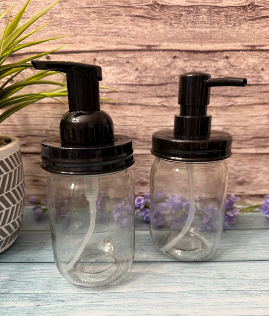 Two clear glass soap dispensers with black pumps on a wooden surface.